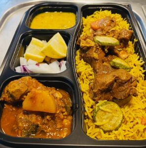 black tray with 4 container food in it. looks like Indian spicy dishes